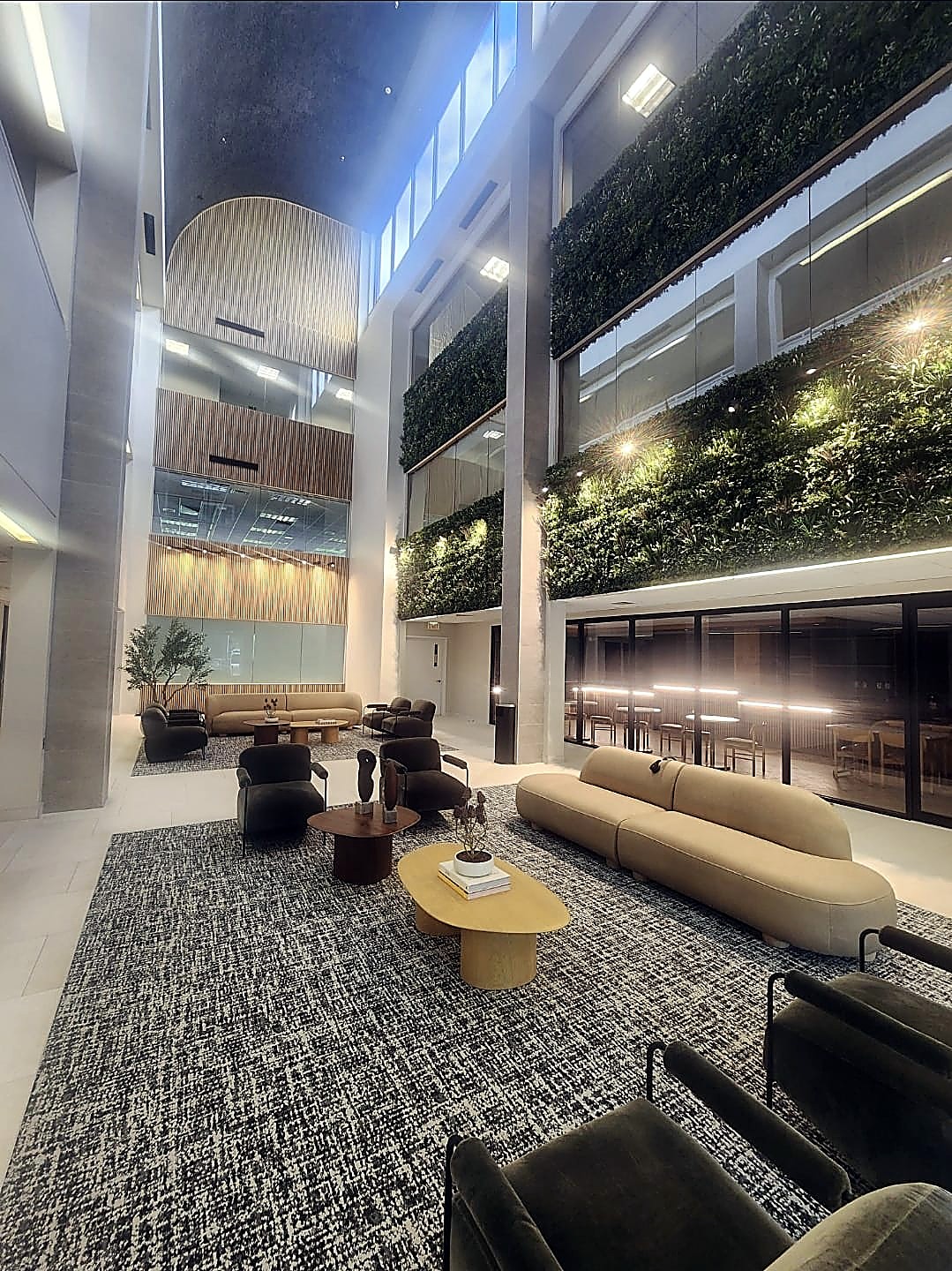 Multi-story commercial office atrium lobby with green walls and lounge seating