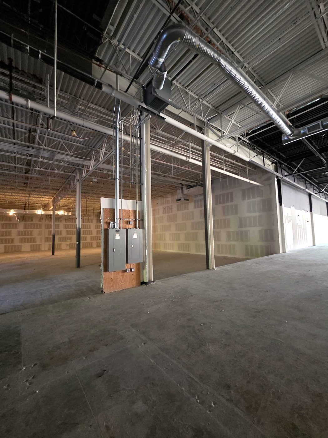 Two electrical panels mounted on plywood in an open warehouse shell