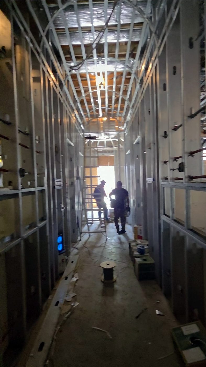 Two electricians in a metal stud corridor during rough-in