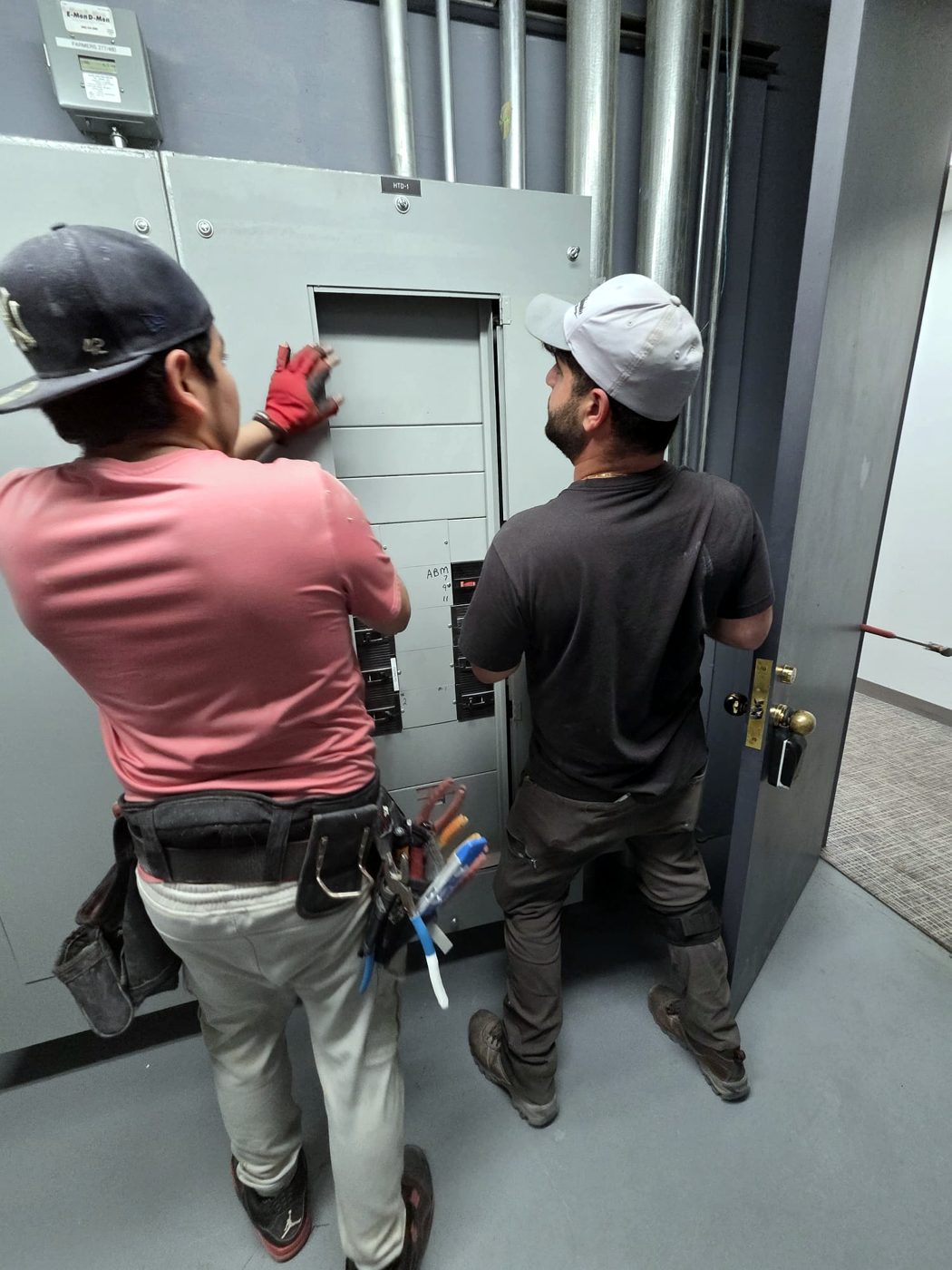 Two electricians working at a panel in an electrical room